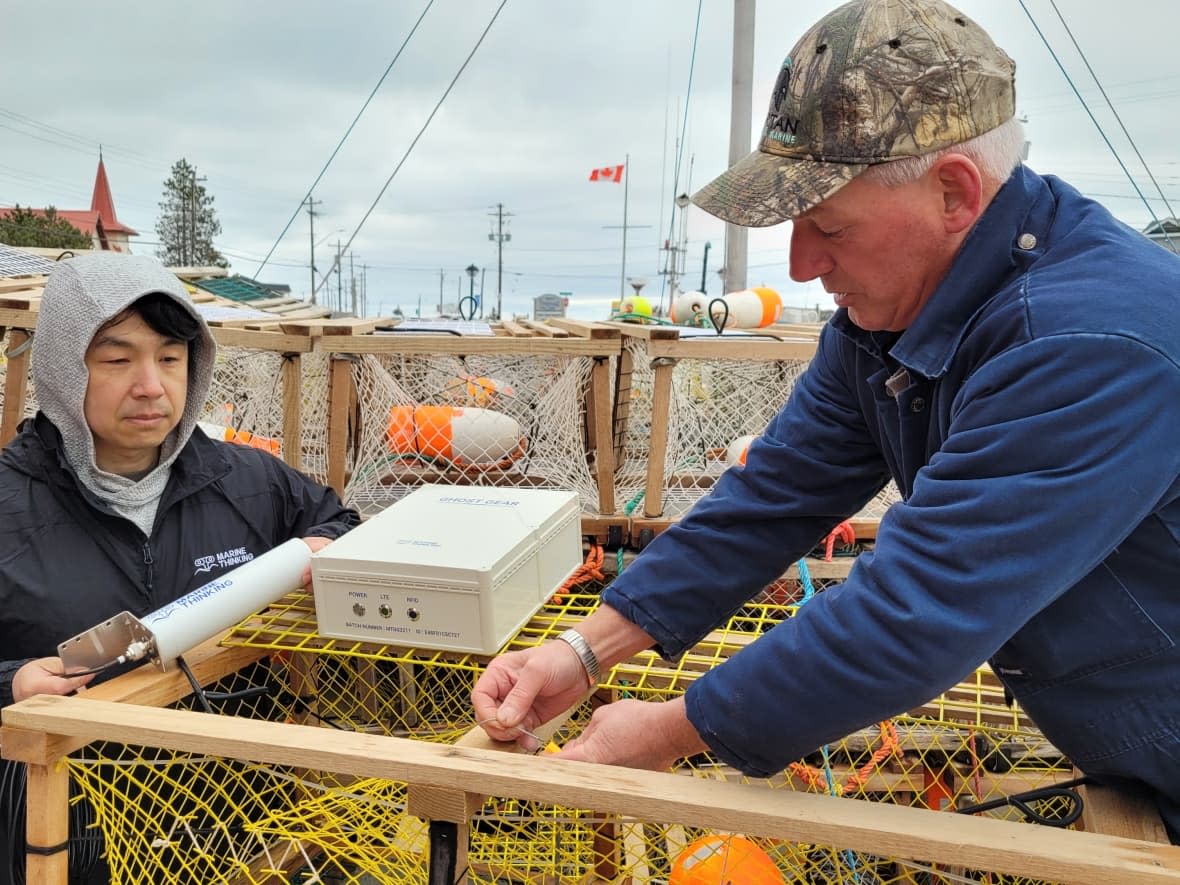 Lobster fisherman Jamie Osborne, right, is shown attaching a tagging device to one of his traps. Yuan Yao, left, is a product director with Marine Thinking. (Gareth Hampshire/CBC - image credit)