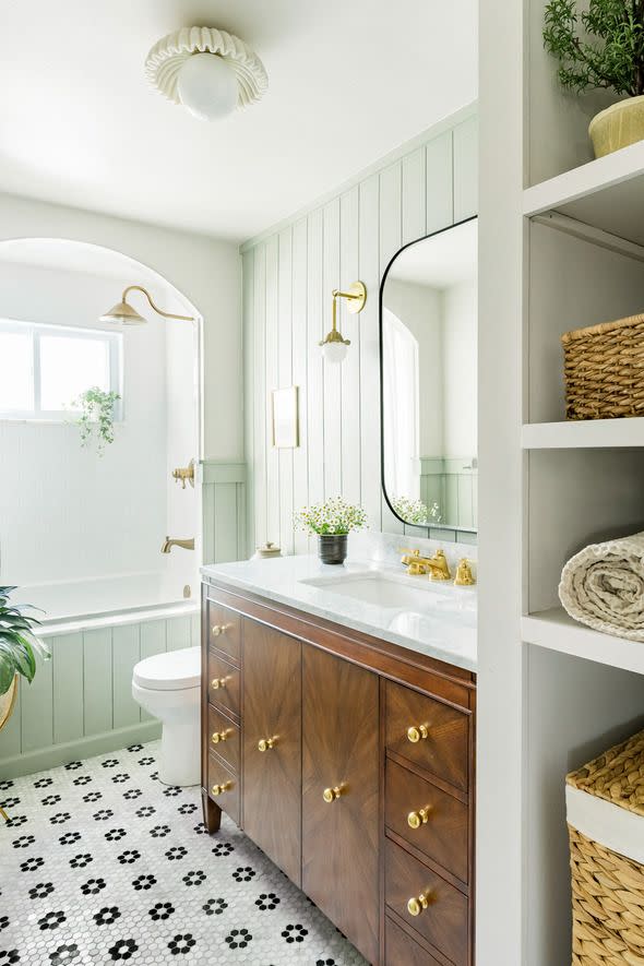 a bright and airy bathroom with a drop in tub, walnut wood vanity, and mirror