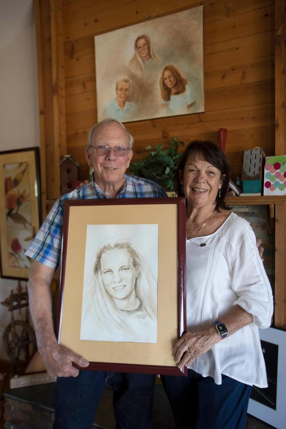 Stan and Denise Smart hold a portrait of their daughter, Kristin, at their Stockton home on May 24, 2023, in front of a painting of their children created by Stan’s sister, Sandy Rudolph.
