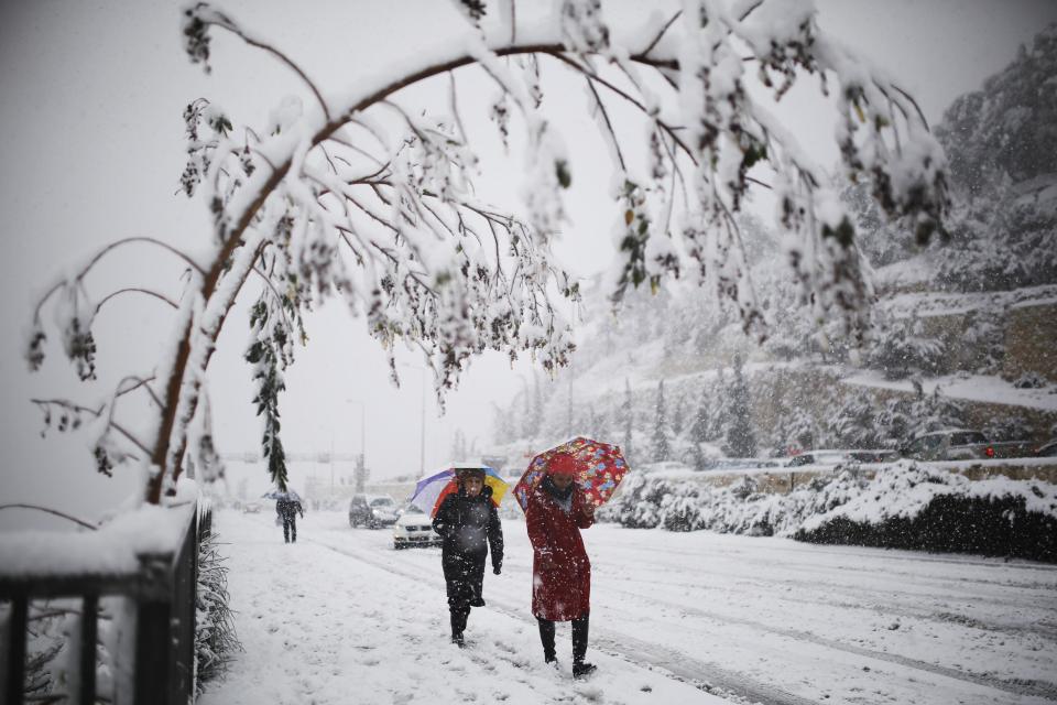 Women walk with umbrellas on a snow-covered road during winter in Jerusalem