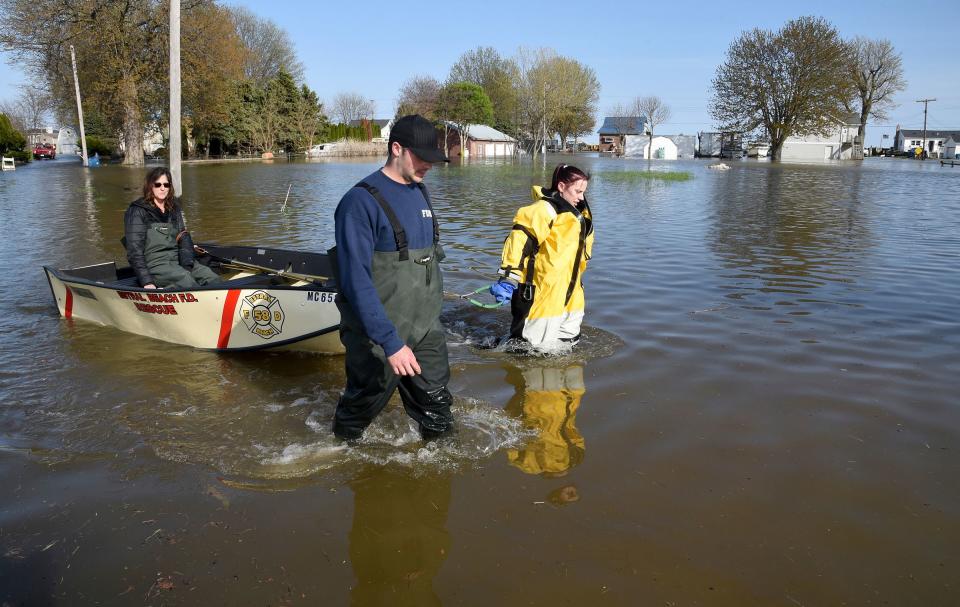 Estral Beach Firefighters Eric Bruley, left, and Courtney Millar wade through waters as they escort Bruley's mother Carla, home after work Wednesday, May 8, 2019 down Lakeshore Dr. in the south end of Estral Beach in Berlin Township, Michigan.