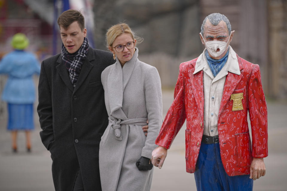 A couple walks by a statue with a face mask on at the Prater amusement park in Vienna, Austria, Sunday, Nov. 21, 2021. The Austrian government announced a nationwide lockdown that will start Monday and comes as average daily deaths have tripled in recent weeks and hospitals in heavily hit states have warned that intensive care units are reaching capacity.(AP Photo/Vadim Ghirda)