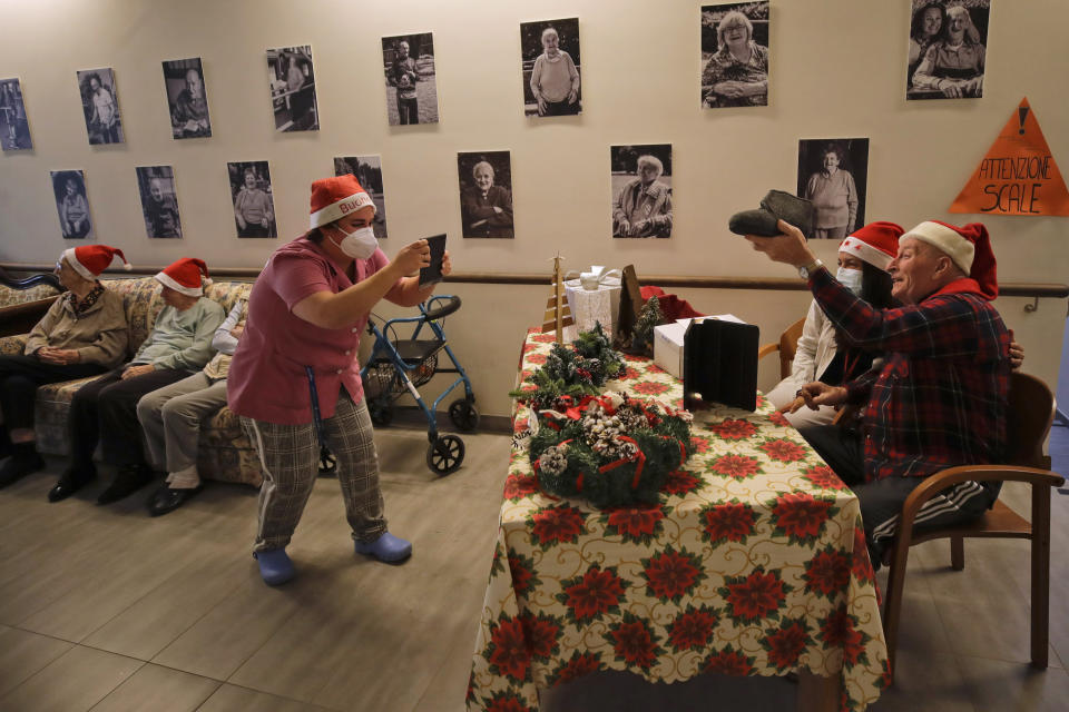 Giuseppe Vitali, right, is flanked by carer Gaia as he is pictured by carer Melania Cavalieri during a video call with Manuela Diana, a donor unrelated to her, who bought and sent her a Christmas present through an organization dubbed "Santa's Grandchildren", at the Martino Zanchi nursing home in Alzano Lombardo, one of the area that most suffered the first wave of COVID-19, in northern Italy, Saturday, Dec. 19, 2020. (AP Photo/Luca Bruno)