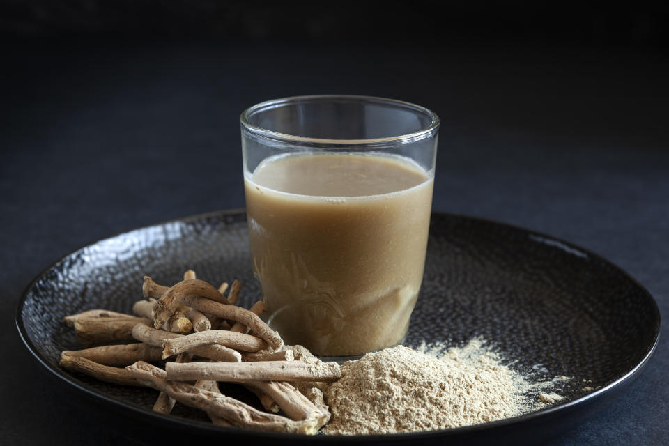 Ashwagandha-Wurzel gemahlen zusammen mit Glas auf schwarzem Tablett.