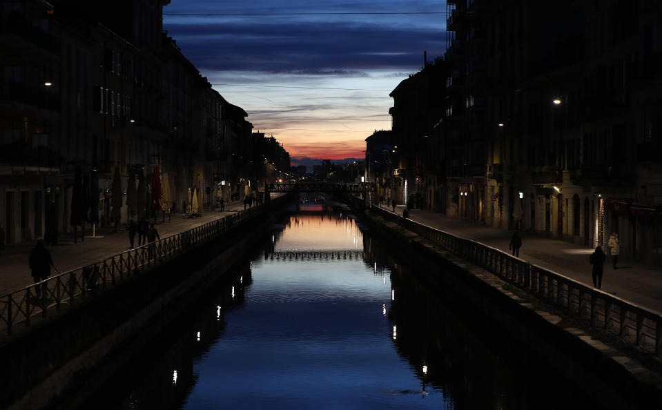 Few people walk at the Naviglio Grande canal, one of the favorite spots for night life in Milan, Italy, Tuesday, March 10, 2020. Italy entered its second day under a nationwide lockdown after a government decree extended restrictions on movement from the hard-hit north to the rest of the country to prevent the spreading of coronavirus. (AP Photo/Antonio Calanni)