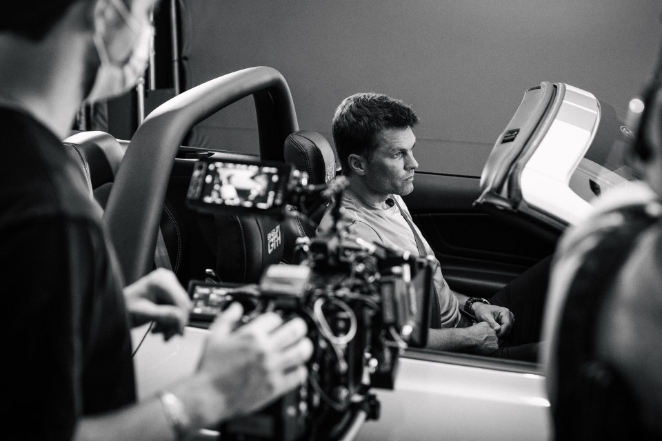 Tom Brady is being filmed in the car on the set of a Hertz commercial.
