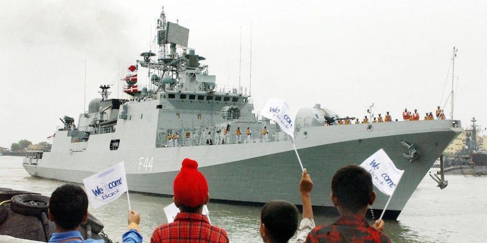 Four children wave flags saying 'welcome back' in front of India's Tabar stealth frigate in Bombay, on 31 July 2004