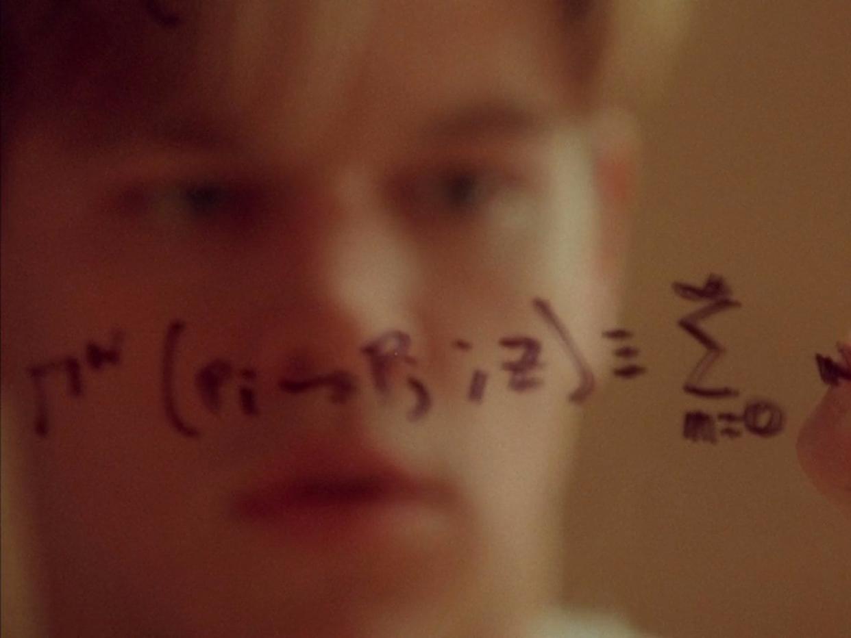 matt damon's reflection is visible through glass with complex equations scribbled on it