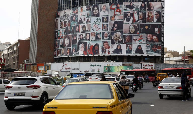 Un grupo de iraníes pasa por delante de una enorme valla publicitaria que muestra un montaje de imágenes titulado "Las mujeres de mi tierra, Irán", con mujeres iraníes que llevan el hiyab, en la plaza Valiasr de Teherán, el 13 de octubre de 2022.