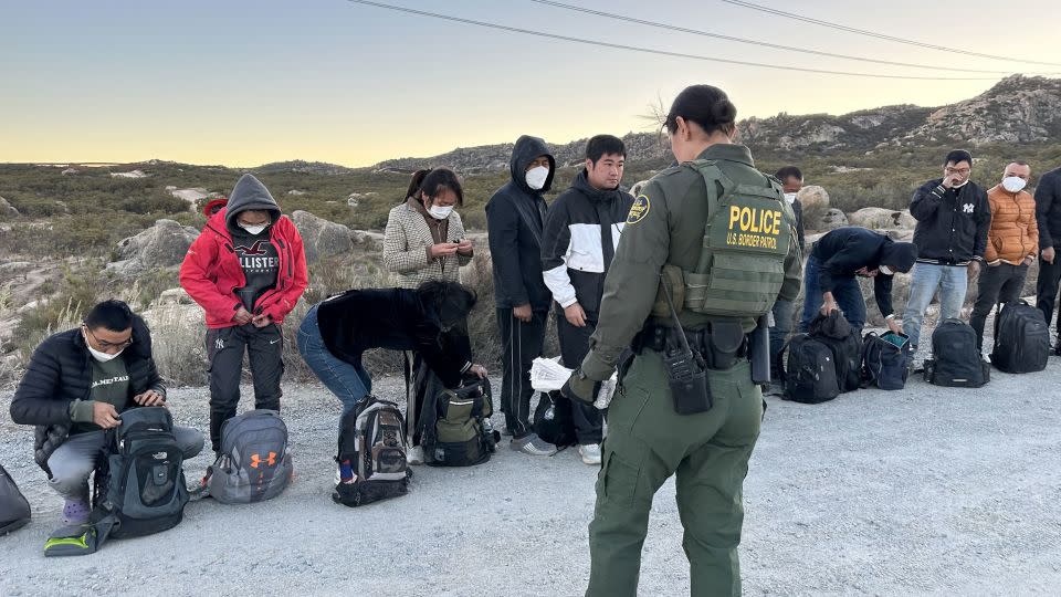 US Border Patrol agent talk to migrants as they await processing at the US-Mexico border in San Diego County. - Norma Galeana/CNN