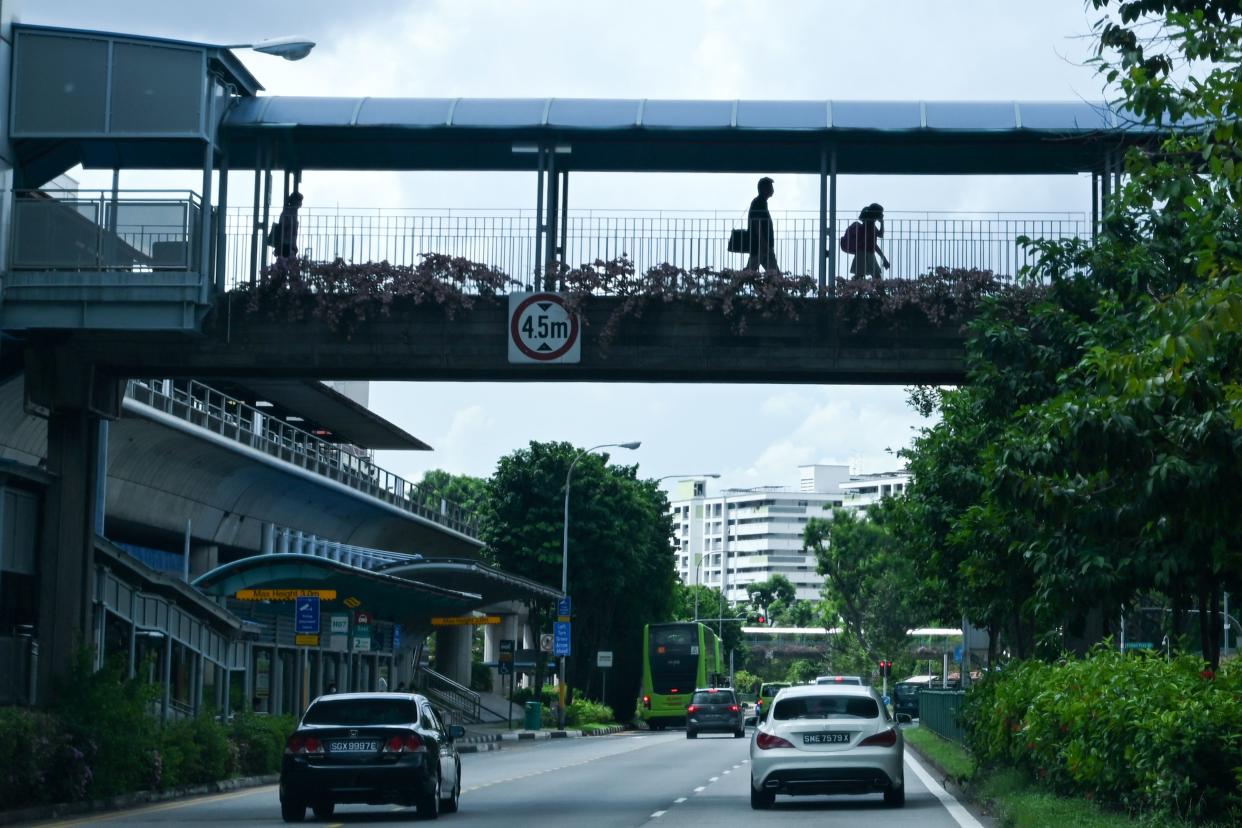 People walk across a pedestrian bridge connected to a train station in Singapore. 