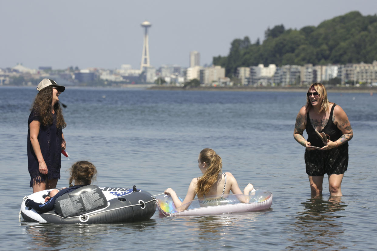 People wade and float on inflatable tubes in water with the Space Needle building in the background.