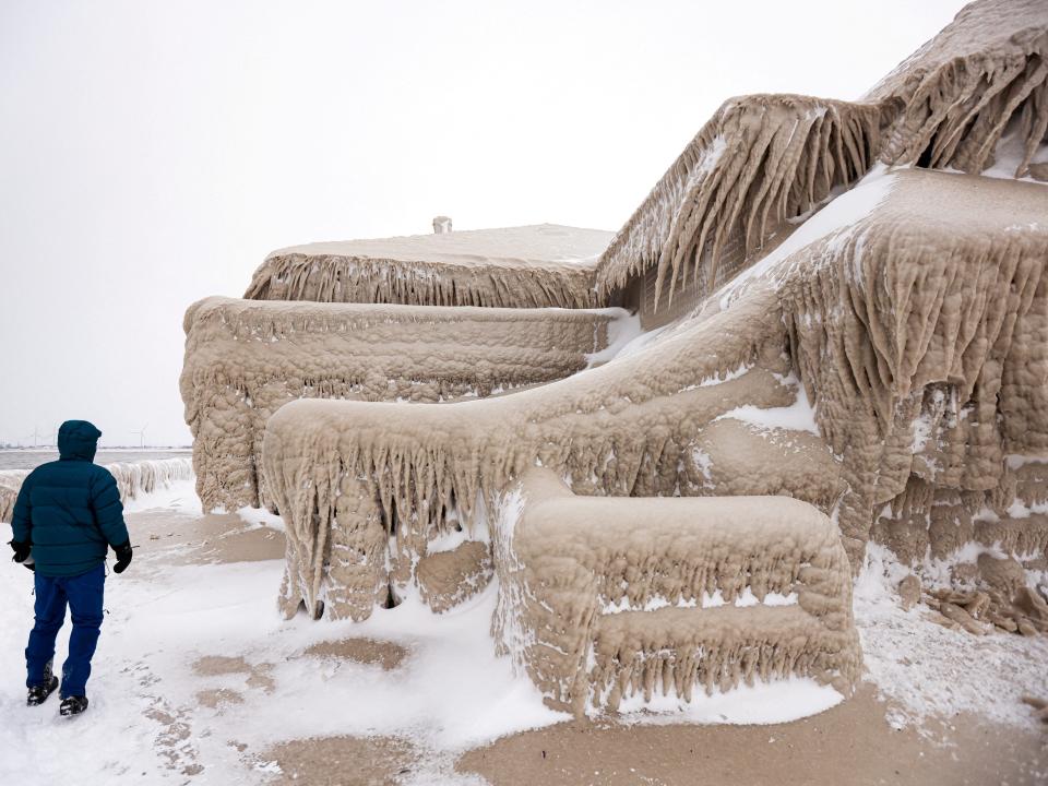 A man walks beside ice formed by the spray of Lake Erie waves which covered a restaurant during a winter storm in Hamburg, New York, U.S., December 26, 2022.