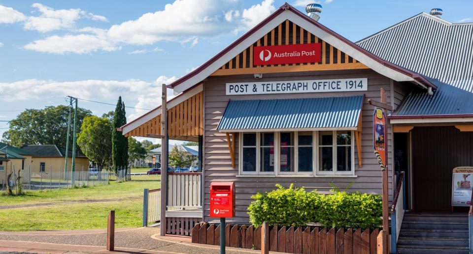 The outside of a post office with a red post box and hedges seen. 