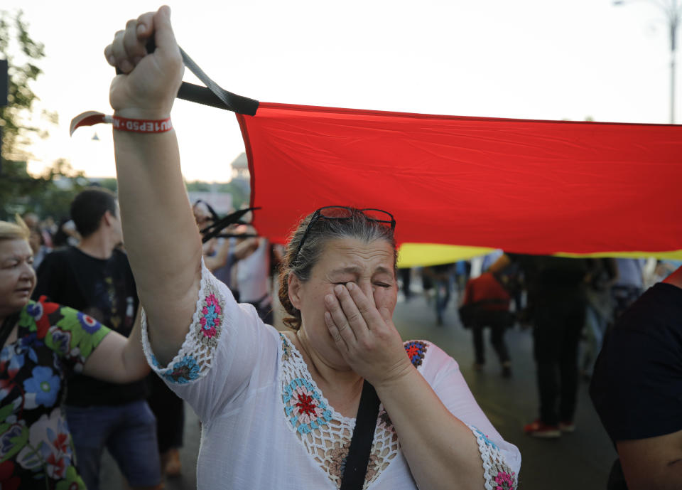 A woman cries holding a large Romanian flag as she take part in a march from the government headquarters in memory of a 15 year-old girl, raped and killed in southern Romania, after police took 19 hours from the moment she called the country's emergency hotline to intervene, in Bucharest, Romania, Saturday, July 27, 2019. Thousands of people took part Saturday evening in Bucharest in a march protesting the handling of the case, blaming Romanian officials for negligence, incompetence and a lack of empathy. (AP Photo/Vadim Ghirda)