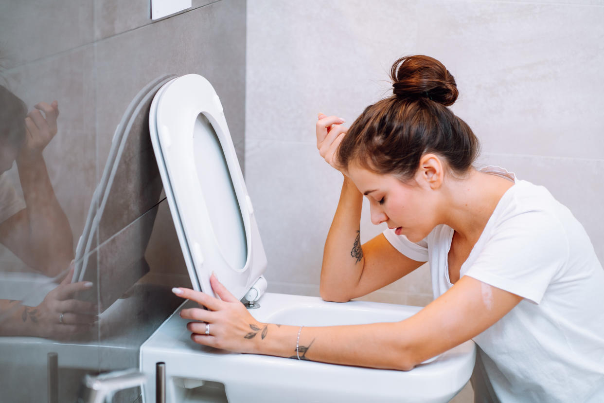 Young woman with hair bun holding her head in bathroom. Eating disorder