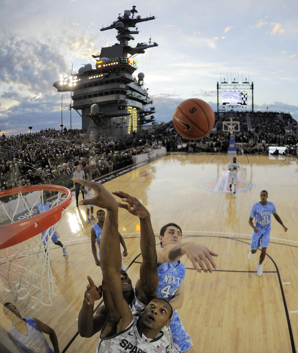 FILE - In this Nov. 11, 2011, file photo, in this image taken with a fisheye lens, North Carolina forward Tyler Zeller (44) swats the rebound away from Michigan State center Adreian Payne, bottom, during the first half of the Carrier Classic NCAA college basketball game aboard the USS Carl Vinson in Coronado, Calif., Nov. 11, 2011. The second “Field of Dreams” baseball game is Thursday night, Aug. 11, 2022, in the cornfields of eastern Iowa, near the site of the beloved 1989 movie. If Major League Baseball is looking for another place for a game, oh man, do we have some fun ideas. (AP Photo/Mark J. Terrill, File)