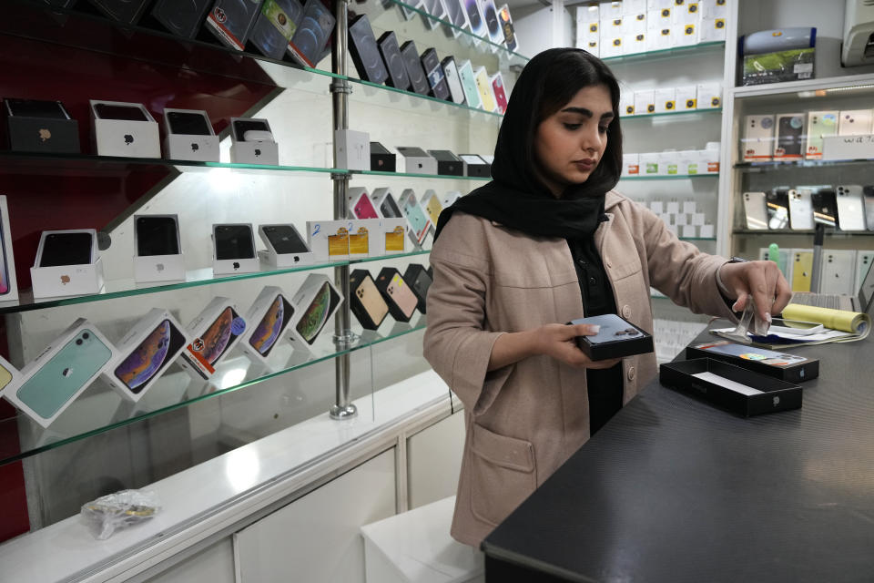 A cellphone vendor works at her shop in downtown Tehran, Iran, Wednesday, Feb. 21, 2024. Even though Supreme Leader Ayatollah Ali Khamenei has denounced American luxury goods amid years of tensions with the West, consumers still want the phones and the prestige associated with them. (AP Photo/Vahid Salemi)