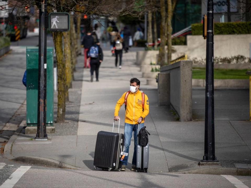 A man wearing a face mask is pictured with luggage in downtown Vancouver, British Columbia in April.  (Ben Nelms/CBC - image credit)