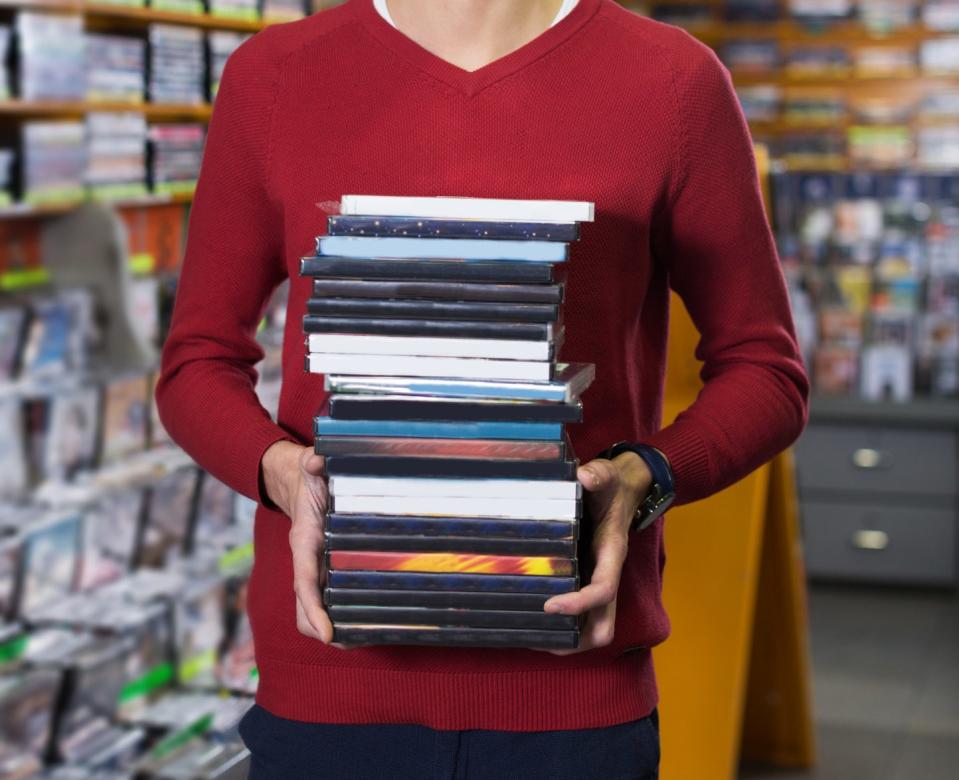 A person holding a stack of DVDs in a rental store