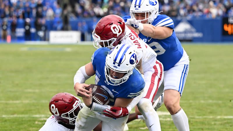 BYU quarterback Jake Retzlaff (12) scores a touchdown as he is hit by Oklahoma Sooners defensive lineman R Mason Thomas (32) and defensive back Woodi Washington (5) as BYU and Oklahoma play at LaVell Edwards Stadium in Provo on Saturday, Nov. 18, 2023.