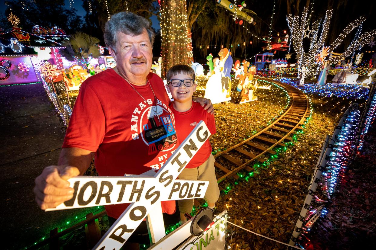 Bill Bigda and his Logan Bigda stand in front of their Bigda Family Santa's House on Shadow Wood Trail  in Winter Haven Fl. Tuesday December 15  2021. Winter Haven's Bigda family put together more than 100,000 Christmas light display for charity. ERNST PETERS/ THE LEDGER