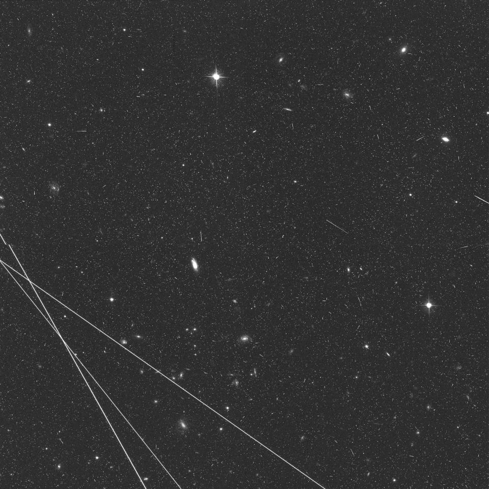 three white satellite lines streak across black and white image of starry universe