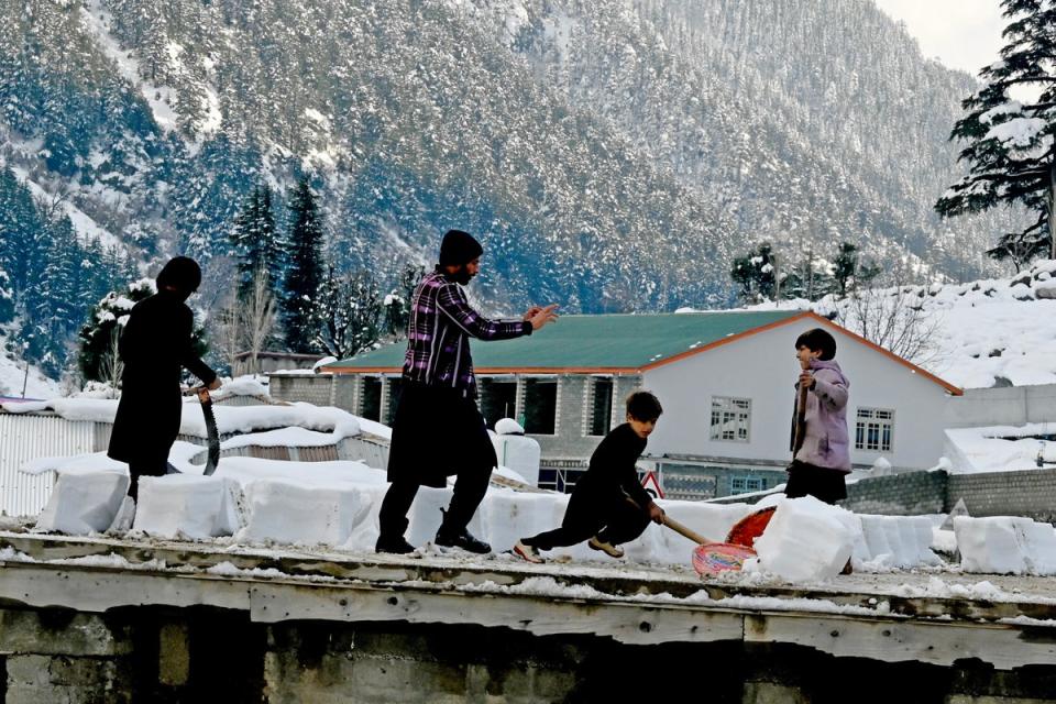 Boys remove snow from the roof of their house in Kalam on 4 March 2024 (AFP via Getty Images)