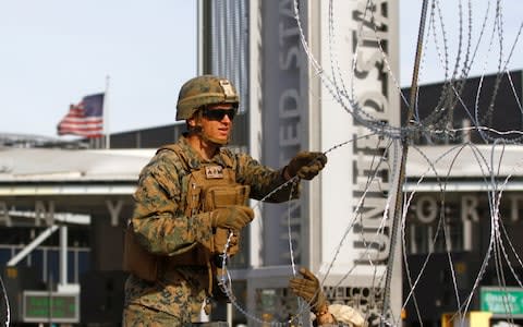 A US Marine sets up a barricade with wire at the border between Mexico and the US in Mexico - Credit: Reuters
