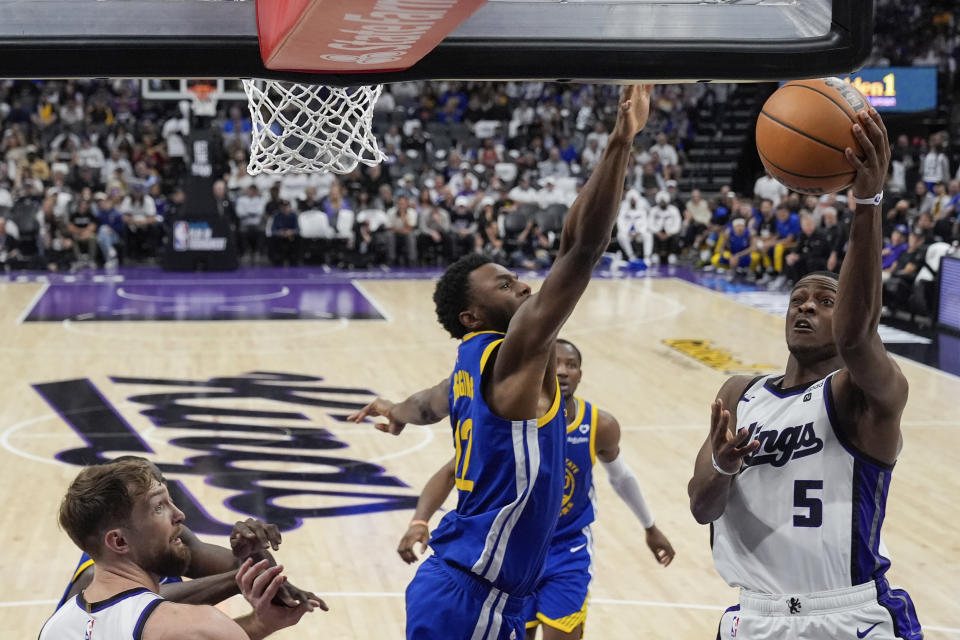 Sacramento Kings guard De'Aaron Fox (5) shoots while defended by Golden State Warriors forward Andrew Wiggins (22) during the second half of an NBA basketball play-in tournament game Tuesday, April 16, 2024, in Sacramento, Calif. (AP Photo/Godofredo A. Vásquez)