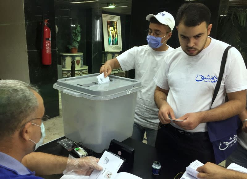 A man wearing a face mask casts his vote inside a polling station during the parliamentary elections in Damascus