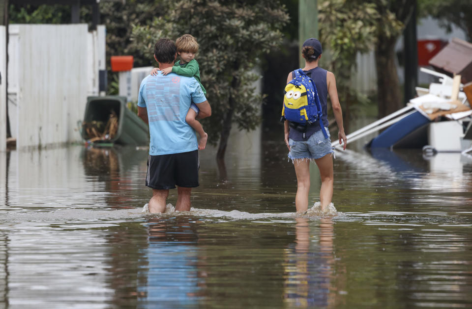 A man carries a child through floodwaters. People are warned to be on the lookout for flood scams.