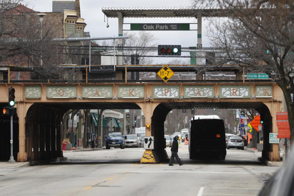 A man walks under the Chicago Transit Authority train station in the Village of Oak Park, Ill., Friday, March 20, 2020. There are at least three confirmed cases of COVID-19 in Oak Park, just nine miles from downtown Chicago, where the mayor has ordered residents to shelter in place. With so few tests available, surely there are others, says Tom Powers, spokesman for the village of about 52,000 in a metropolitan area with millions. (AP Photo/Charles Rex Arbogast)
