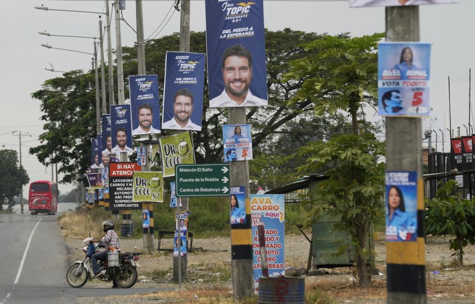 A man rides his motorcycle on a street with political propaganda of presidential candidate Jan Topic hanging from utility posts, in Babahoyo, Ecuador, Tuesday, Aug. 15, 2023. Ecuador's president declared a state of emergency in some areas after a presidential candidate was killed at a rally ahead of snap elections. (AP Photo/Martin Mejia)