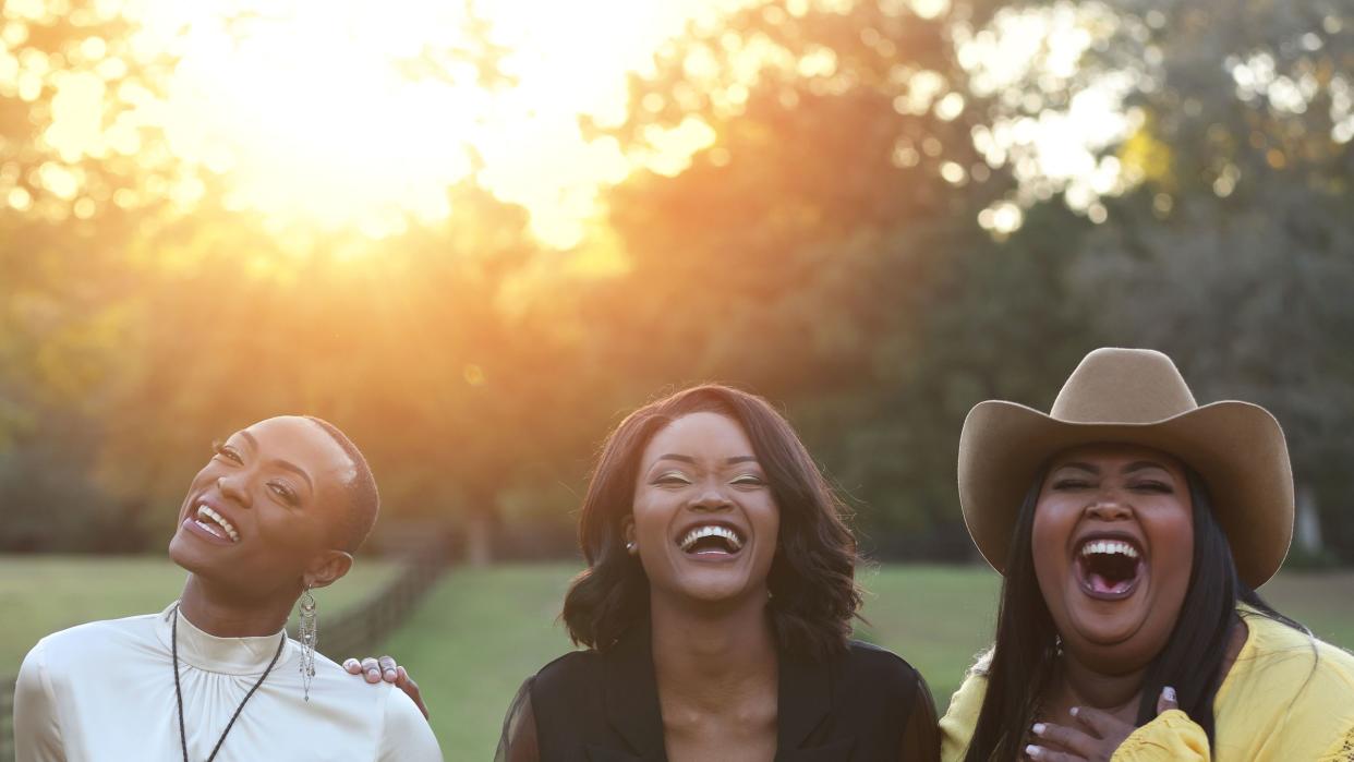 trea swindle, devynn hart and danica hart of chapel hart posing in front of a rustic fence enclosing a pasture