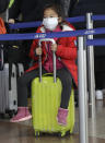 A girl wearing a mask sits on a suitcase while waiting to check-in to a flight to Shanghai at the Vaclav Havel International Airport in Prague, Czech Republic, Monday, Jan. 27, 2020. Prague's international airport is launching an information campaign for travellers who develop symptoms possibly linked to a new coronavirus illness. (AP Photo/Petr David Josek)