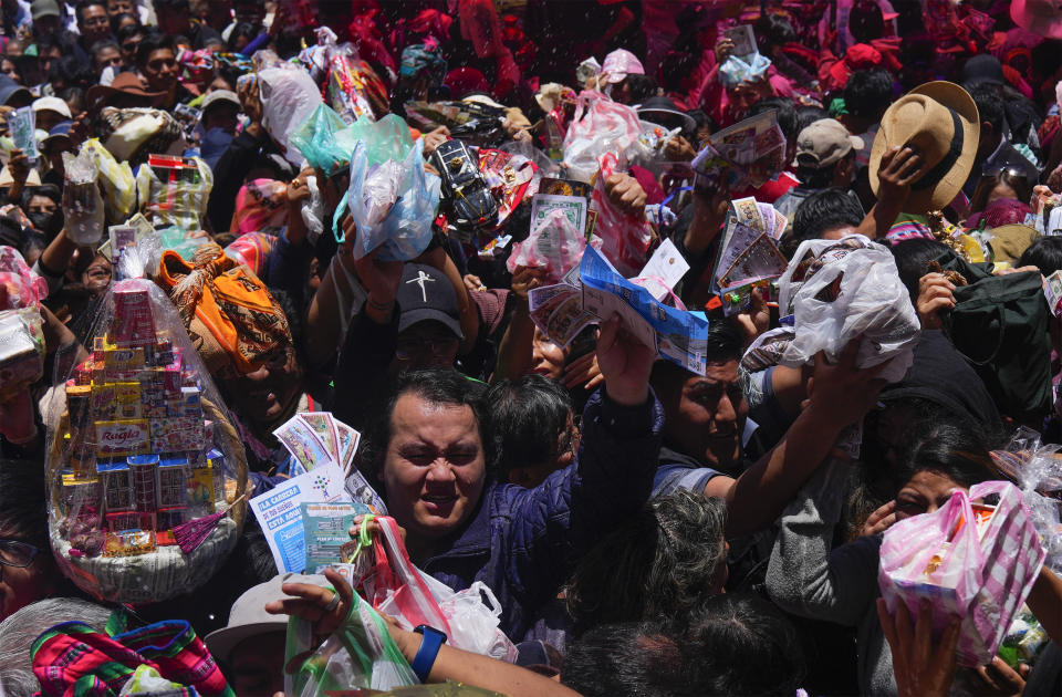 Personas llevan casas en miniatura y billetes falsos a bendecir por un cura católico a las afueras de la iglesia de San Francisco durante la feria anual de Alasita en La Paz, Bolivia, el miércoles 24 de enero de 2024. En el día de inauguración de la feria se ofrecen réplicas en miniatura de las cosas que las personas anhelan o desean, como casas, vehículos o salud, para que se conviertan en realidad. Alasita es una palabra aymara que significa "cómprame". (AP Foto/Juan Karita)