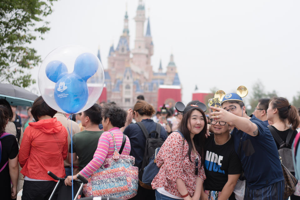 Couple taking a selfie with a crowd and a Disneyland castle in the background