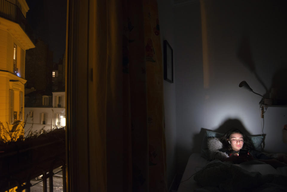 Anais Bulcao, 17, checks her phone in bed on May 18, 2021, in the bedroom that she has had to share with Livia, her eldest sister, since the 23-year-old was forced by the pandemic to stop her travels in Australia and move back in with her family in their apartment in Montmartre, Paris. Anais says the months they spent together in lockdown have become a hazy blur because "the days were all alike." (AP Photo/Joao Luiz Bulcao).