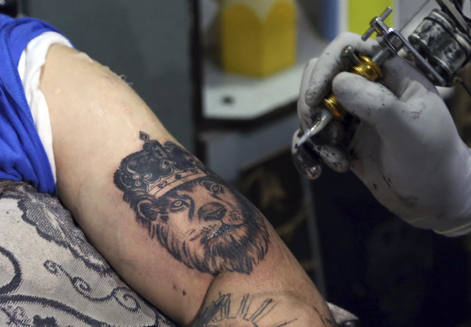 In this Wednesday, Nov. 20, 2019, photo, Omid Noori, 23, left, gets a lion tattoo on his left arm by Nazeer Mosawi, a tattoo artist in Kabul, Afghanistan. Mosawi, 42, fought for seven years in Afghanistan’s civil war with the Islamic insurgents. He says he is still fighting the war, but this time his battle is against society’s conservatism, with his tattoo machine as his weapon.(AP Photo/Rahmat Gul)