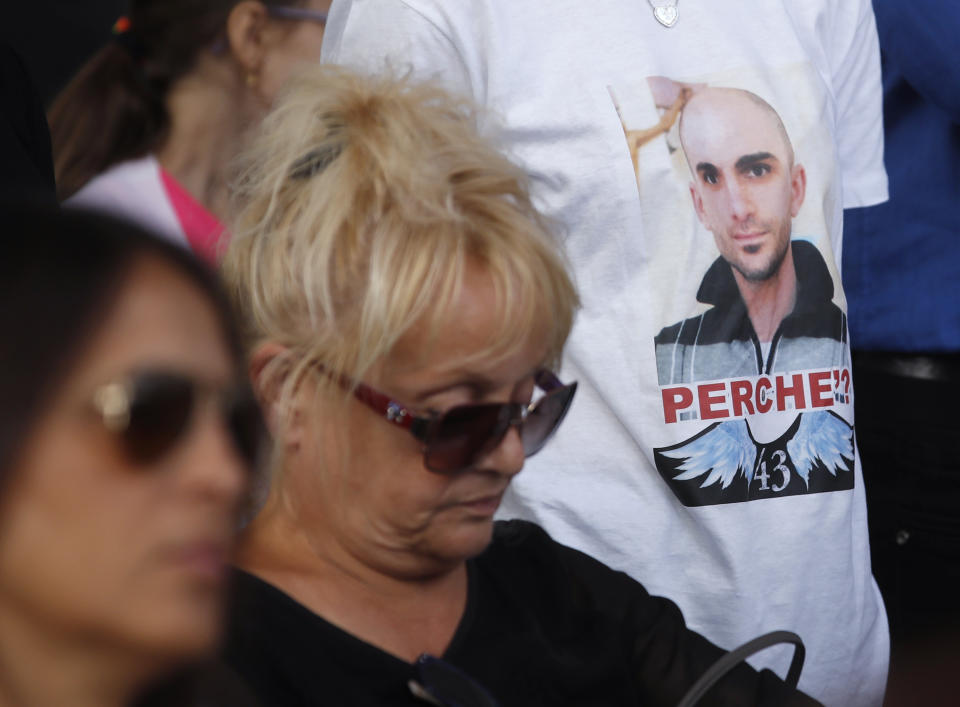 Relatives of the victims of the Morandi bridge collapse, attend a remembrance ceremony to mark the first anniversary of the tragedy, in Genoa, Italy, Wednesday, Aug. 14, 2019. The Morandi bridge was a road viaduct on the A10 motorway in Genoa, that collapsed one year ago killing 43 people. On the shirt at right is portrayed one of the victim with the writing "Why?". (AP Photo/Antonio Calanni)
