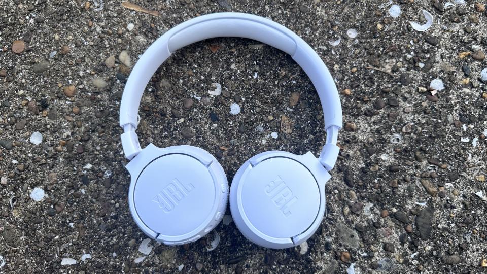 The JBL Tune 670NC over-ear headphones in white pictured on grey concrete.