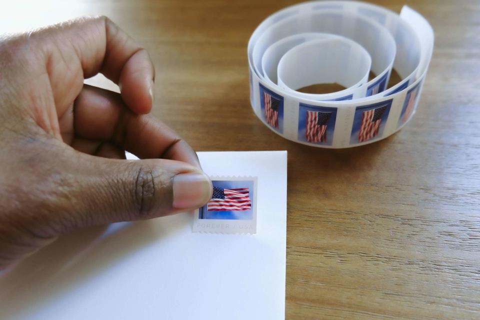 <p>Getty</p> Stock image of a woman placing postage stamp on envelope