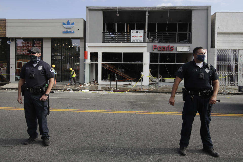 Police officers stand in front of a fire-damaged building, Sunday, May 31, 2020, in Los Angeles, following a night of unrest and protests over the death of George Floyd, a black man who was in police custody in Minneapolis. Floyd died after being restrained by Minneapolis police officers on May 25. (AP Photo/Marcio Jose Sanchez)