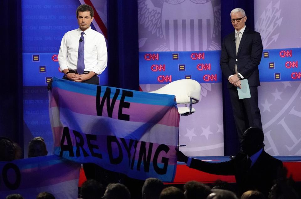 Democratic presidential candidate, South Bend, Indiana Mayor Pete Buttigieg (L) and CNN moderator Anderson Cooper react as protestors display banners, protesting deadly violence against transgender women of color, at the Human Rights Campaign Foundation and CNN’s presidential town hall focused on LGBTQ issues on October 10, 2019.