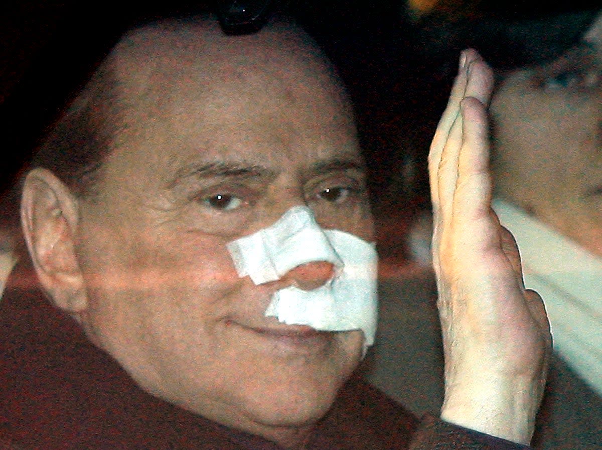 Berlusconi waves from his car as he arrives at his home, with his face covered in bandages, four days after an attack at a political rally in December 2009 (AP)