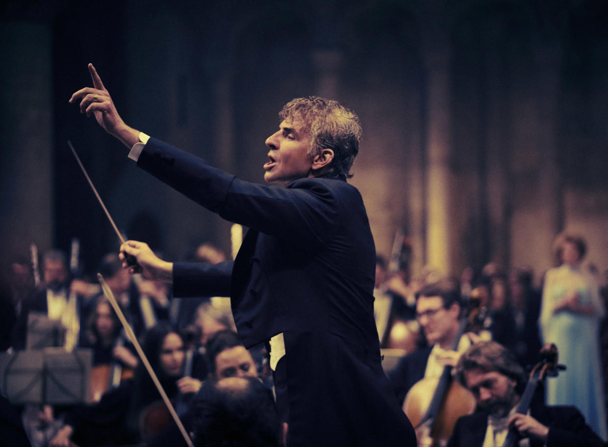 Bradley Cooper, portraying Leonard Bernstein in Maestro, conducts an orchestra.