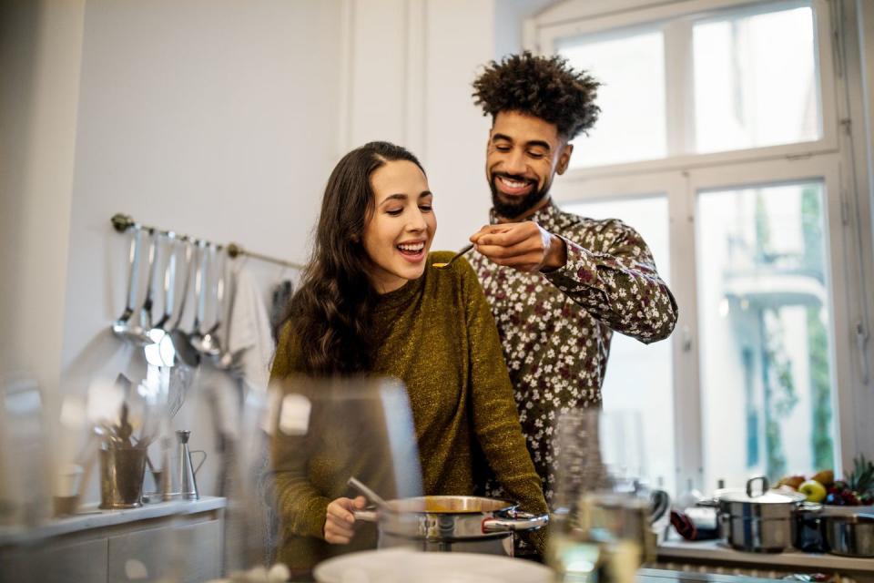 man feeding pumpkin soup to girlfriend in kitchen