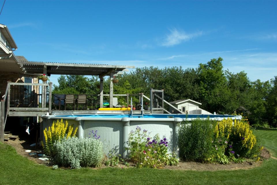 A backyard deck with a nearby above-ground swimming pool surrounded by plants