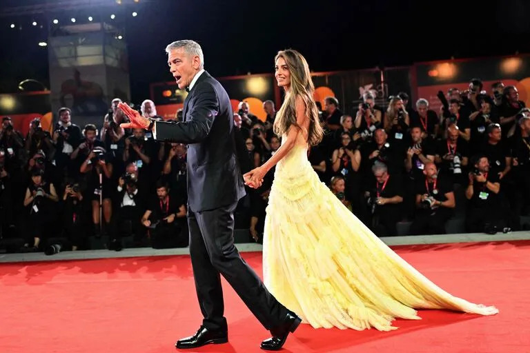 George Clooney y su mujer, Amal Clooney, le aportaron brillo y glamour a la alfombra roja. Si bien el actor de 63 años se destacó con un elegante traje negro, todas las miradas se posaron en la figura de la abogada de derechos humanos, quien eligió uno de los colores más celebrados del verano europeo: el amarillo manteca. El diseño, de Versace, incluyó una falda larga con cola de volados y tul y un corset adornado con encaje